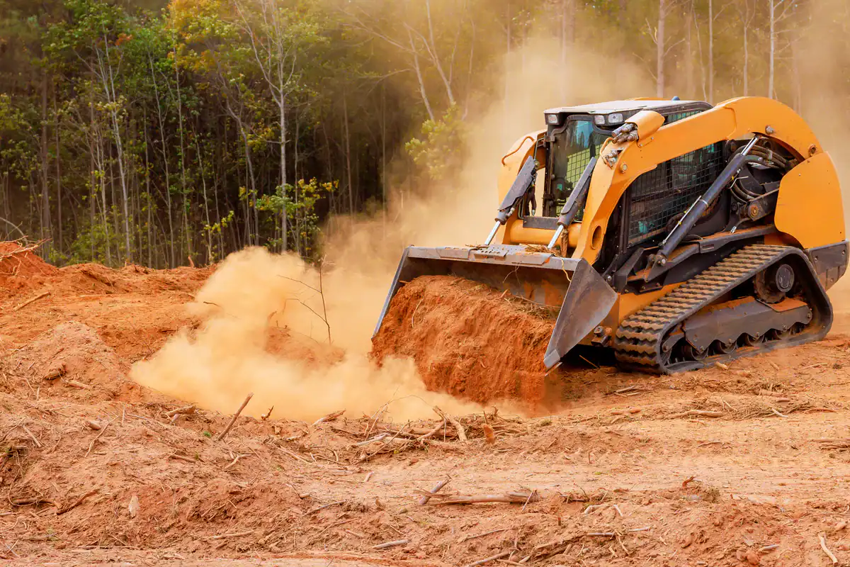 A yellow bulldozer moves dirt to assist tree removal on a Kansas City Metropolitan Area site near forests.