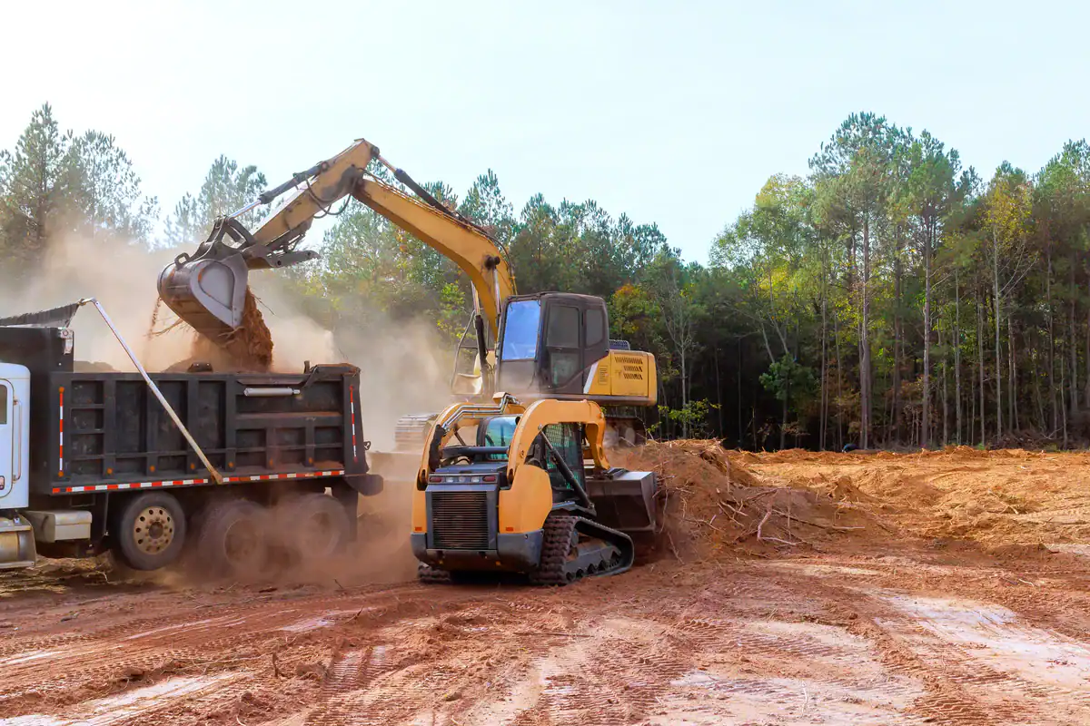 An excavator loads dirt as a bulldozer works nearby on a dusty site in the Kansas City Metropolitan Area.